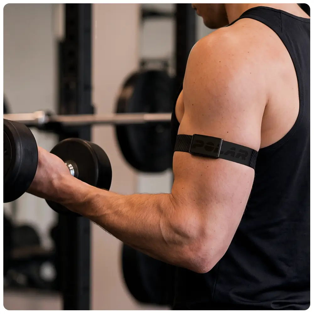 Lifestyle-Aufnahme eines Mannes im Fitnessstudio beim Hanteltraining. Am rechten Oberarm trägt er den POLAR Loop Tracker in einer speziellen Halterung an einem breiten, elastischen Textilarmband in Dunkelgrau.