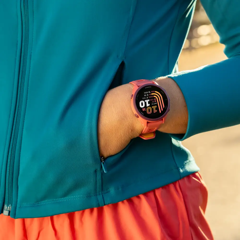 Nahaufnahme der Garmin Forerunner 170 Music Smartwatch am Handgelenk einer Sportlerin in einer blau-orangefarbenen Laufkombination