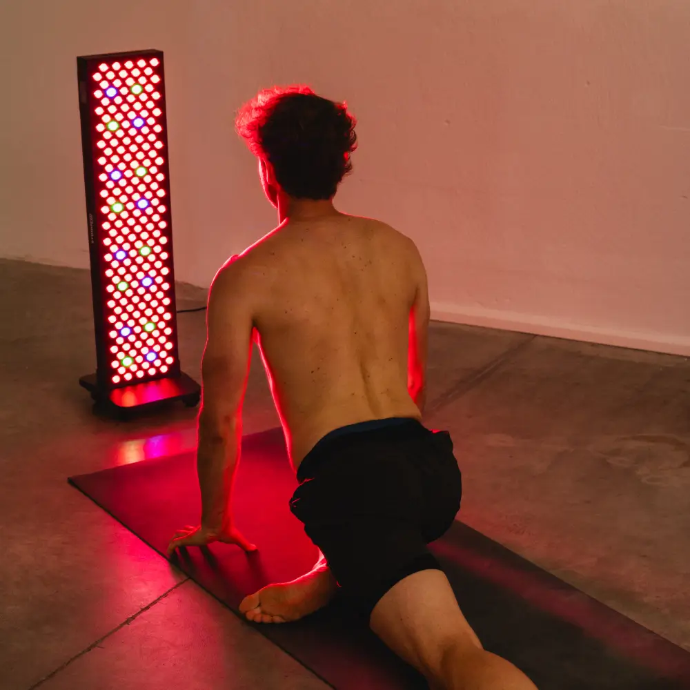 Ein Sportler dehnt sich in einer Yoga-Pose (Kobra) auf einer Matte vor dem großen, bunt leuchtenden Reboots Relight Pro Rotlicht-Standpanel.