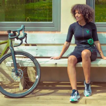 Antelope EMS-Anzug an einer Radfahrerin neben einem Rennrad – kabelloses EMS-Training zur Unterstützung von Muskelaufbau, Kraftausdauer und Leistungssteigerung im Radsport.
