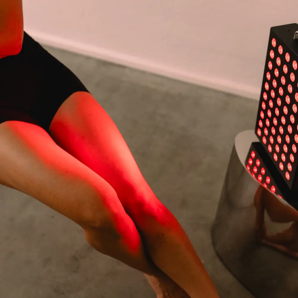 Gezielte Rotlicht-Anwendung des Reboots Relight Mini Panels auf die Knie und Beine einer Sportlerin im Sitzen.